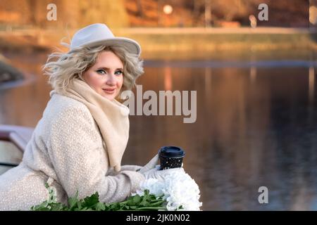 Ritratto di una donna bionda in un cappello con occhio luminoso trucco in autunno nei raggi del sole tramontare sullo sfondo della natura - acqua e fuchi Foto Stock