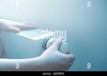 La giovane donna regola la temperatura del suo radiatore durante la stagione di riscaldamento, prezzi elevati di energia e concetto di crisi economica Foto Stock