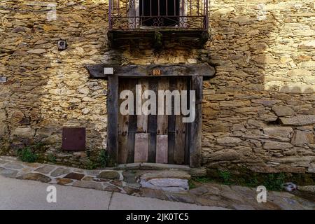 Facciata di una casa molto antica con una porta in legno e un balcone con barre di ferro. La Hiruela Madrid. Spagna. Foto Stock