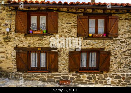 Vecchia facciata in pietra con quattro finestre in legno e le loro persiane. Madrid. La Hiruela. Foto Stock