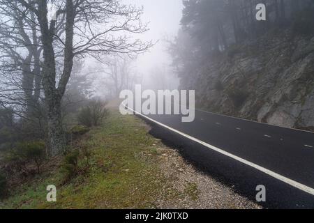 strada di montagna curva in una giornata densa di nebbia con visibilità molto bassa. Morcuera, Spagna. Foto Stock