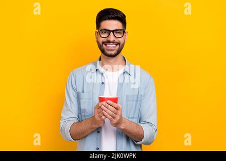 Foto del bel giovane latino che ha break time out tenere tazza indossare elegante abito denim occhiali isolati su sfondo giallo Foto Stock