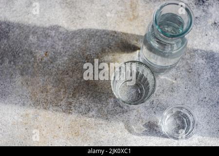 Acqua pura sana in bottiglia e bicchieri su tavola di cemento grigio Foto Stock