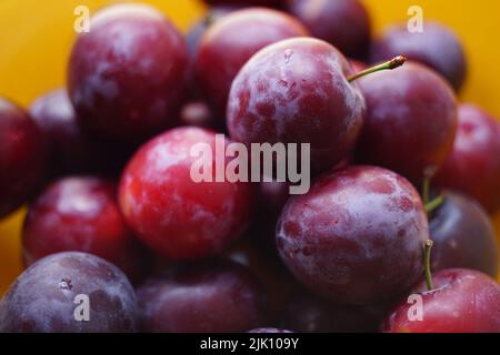 Prugne mature primo piano in piatto d'arancia, fresco cibo estivo Foto Stock