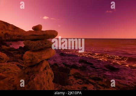 Piramide della felicità. Le pietre piatte sono impilate dai beachgoers sulla riva del mare sotto forma di una piramide. Foto a infrarossi impressionista Foto Stock