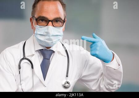 il medico maschile che indossa una maschera medica e guanti medici sta gesturando per la sua attrezzatura igienica Foto Stock