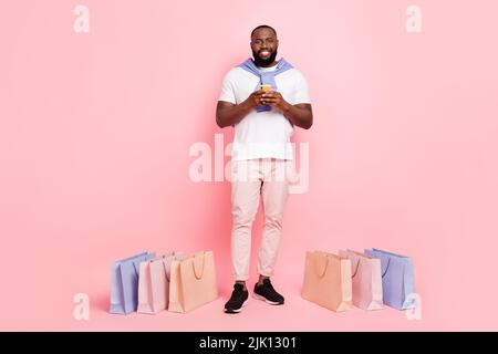 Full body image of Young male surfing in negozio online acquistare molti abiti alla moda isolato su sfondo rosa Foto Stock