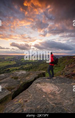 Un camminatore in piedi sul bordo di Curbar al tramonto, Derbyshire, distretto di picco, Derbyshire, Inghilterra, Regno Unito, Europa Foto Stock