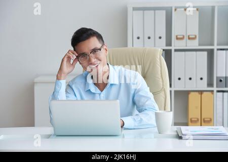 Ritratto di bel giovane uomo d'affari felice al suo tavolo Foto Stock
