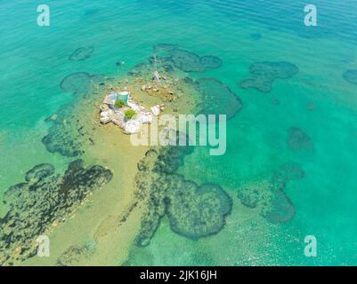 Vista aerea dell'isola vicino alle spiagge di Notos e Petriti Issos a Corfù, Grecia. Piccolo isolotto con bandiera greca e croce vicino alla riva Foto Stock