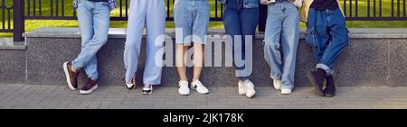 Gambe di sei giovani in eleganti abiti in denim in fila sulla strada della città. Foto Stock