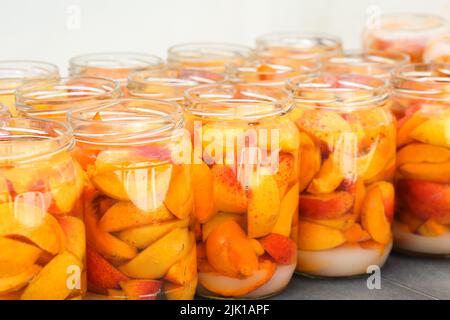 Primo piano di fette di albicocca con acqua e zucchero in vasetti. I compote di frutta fatti in casa sono pronti per essere lisati e sterilizzati. Preparazione di forniture invernali a casa. Foto Stock