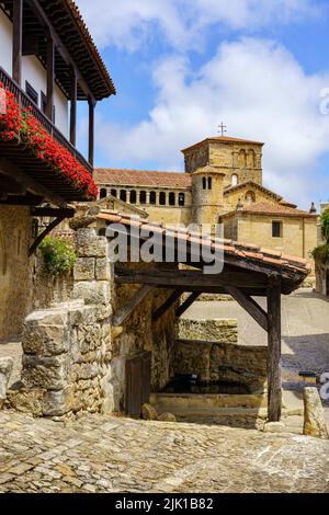 Fontana d'acqua con tetto e chiesa sullo sfondo in un antico borgo medievale. Santillana del Mar, Santander. Foto Stock