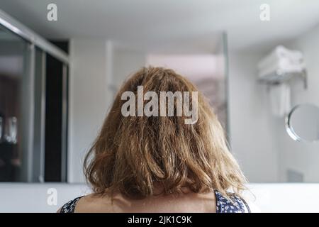 Donna da dietro guardando lo specchio in un bagno per pettinarle i capelli. Spagna. Foto Stock