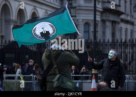 Una persona che indossa una maschera è circondata da fotografi durante una protesta contro il costo della crisi vivente vicino Downing Street a Londra. Foto Stock