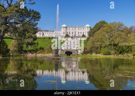 Irlanda, Contea di Wicklow, Enniskerry, Powerscourt Estate House and Gardens, Powerscourt House riflesso nel lago Triton con fontana sparare in aria. Foto Stock