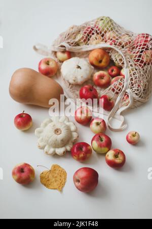 raccolta autunnale con sqush, zucca, mele e verdure in una borsa a rete su sfondo bianco Foto Stock