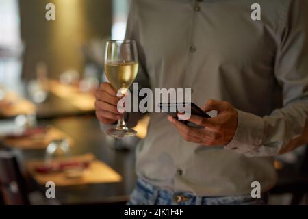 Immagine ritagliata dell'uomo che beve un bicchiere di vino e controlla messaggi di testo Foto Stock