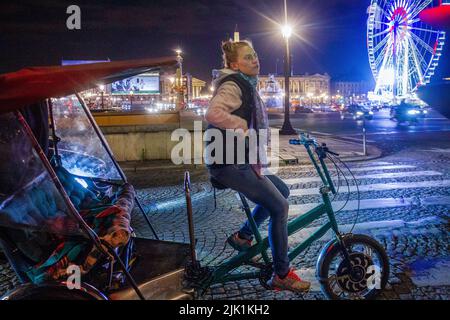 14-05-2016 PARIGI, Francia. Una giovane donna è un risciò (che parla). Aspetto europeo, e una ruota Ferris sullo sfondo di pietre di notte e pavimentazione Foto Stock