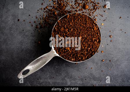 Caffè macinato grossolanamente in una tazza graduata: Caffè appena macinato che trabocca di una tazza graduata Foto Stock