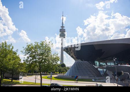 Monaco di Baviera, Germania - 6 luglio 2022: Vista oltre la facciata di vetro del BMW World al Parco München Olympia con la Torre Olympia (Olympiaturm). La Torre serve Foto Stock