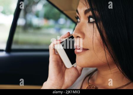 Immagine ravvicinata della giovane donna che chiama al telefono quando si siede in taxi Foto Stock
