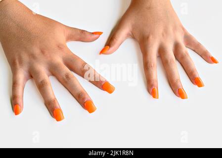 Le mani della ragazza con le unghie false arancioni. Manicure della donna Foto Stock