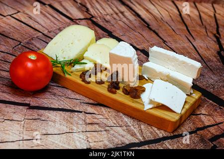 Tavola di formaggi freschi e assortiti di capra, tagliata a spicchi su un asse di legno. Foto Stock