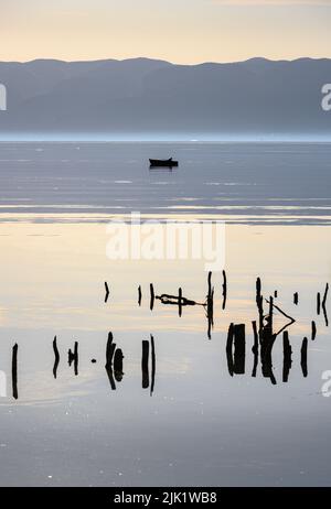 Un pescatore di prestito nella sua barca a remi sul lago di Ohrid a Peshtani nel nord della Macedonia, con l'Albania in distanza, Nord Macedonia, l'Europa. Foto Stock