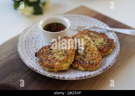 Frittelle di zucchine, frittelle di zucchine vegetariane su un piatto bianco servito con salsa di soia in un piccolo recipiente bianco. Cibo vegetariano Foto Stock