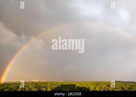 grande arcobaleno nel cielo blu grigio sopra il parco della città illuminato dal sole prima della tempesta di tuono nella giornata estiva soleggiata Foto Stock