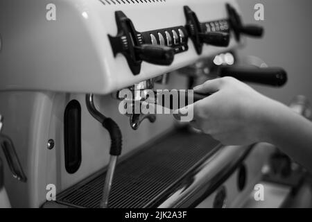 Il barista tiene in mano un portadocumenti e prepara il caffè con una macchina da caffè a doppia caldaia Foto Stock