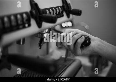 Il barista tiene in mano un portadocumenti e prepara il caffè con una macchina da caffè a doppia caldaia Foto Stock