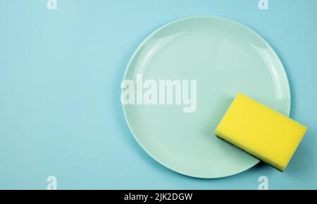 Concetto di piatti di lavaggio. Piatto con spugna su sfondo blu pastello, vista dall'alto Foto Stock