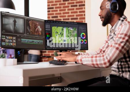 Editor multimediale che utilizza un software per modificare le riprese video su più monitor a casa, modificando i filmati con l'applicazione di produzione sul computer. Lavorare al montaggio su pellicola per creare contenuti multimediali. Foto Stock