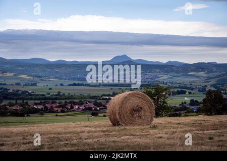 Vista delle montagne in primavera in Auvergne, Francia, da un campo con una balla di paglia Foto Stock