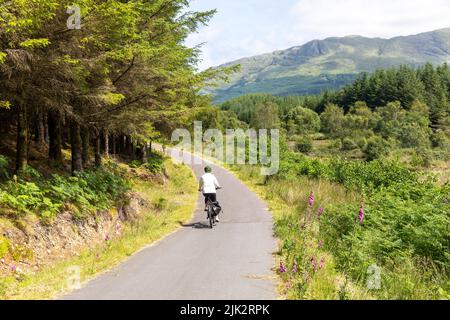 Scozia, modello donna rilasciato in bicicletta sulla Caledonia Way National cycling Route 78 vicino Glencoe, Highlands scozzesi, giorno di sole estate 2022 Foto Stock