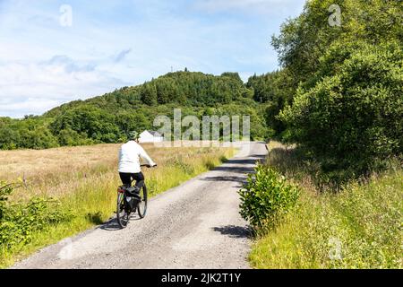 Scozia, modello donna rilasciato in bicicletta sulla Caledonia Way National cycling Route 78 vicino Glencoe, Highlands scozzesi, giorno di sole estate 2022 Foto Stock