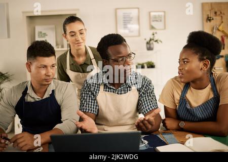 Gruppo di studenti di moda o designer brainstorming e parlare di vestiti, prendendo appunti in libro e laptop. Diversi sartors imparano a conoscere il denim Foto Stock