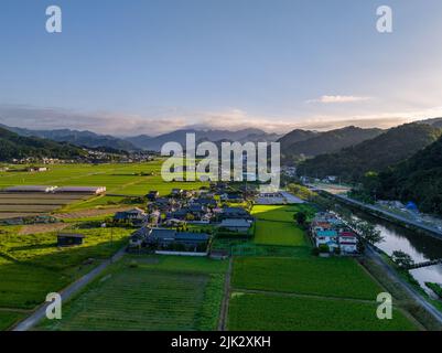 Il sole al mattino presto splende attraverso le montagne su un piccolo villaggio e campi di riso Foto Stock