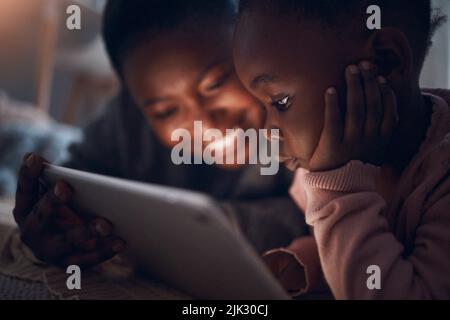 Cosa pensi che succederà dopo. Una madre che legge le storie dell'ora di dormire con sua figlia su un tablet digitale. Foto Stock