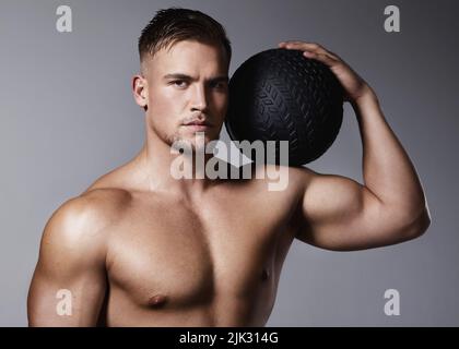 Voglio che tu raggiunga i tuoi obiettivi di fitness. Un giovane sportivo che tiene in mano una palla da ginnastica mentre si trova su uno sfondo grigio. Foto Stock