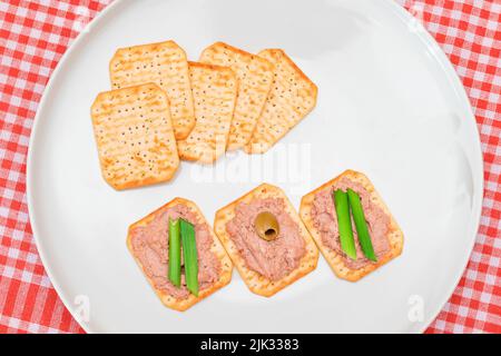 Cracker salati croccanti con patatine al fegato, cipolle verdi e olive su piastra bianca. Snack facile Foto Stock