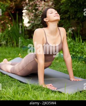 Lo yoga significa mettere la mente e il corpo a proprio agio. Una giovane donna che fa un tratto di cobra mentre si esercita all'aperto. Foto Stock
