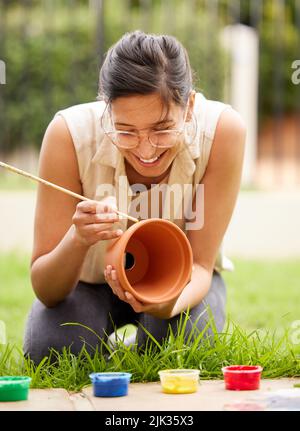 Se volete lavoratori creativi, date loro abbastanza tempo per giocare. S giovane donna che dipinge una pentola in giardino a casa. Foto Stock