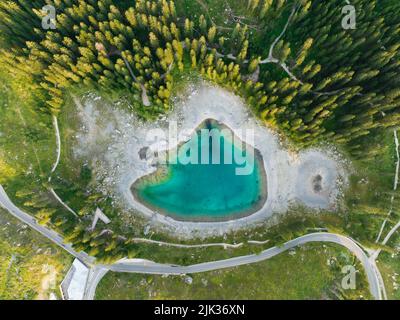 Vista dall'alto, splendida vista aerea del Lago di Carezza (Lago di Carezza) circondato da splendidi alberi al tramonto. Foto Stock