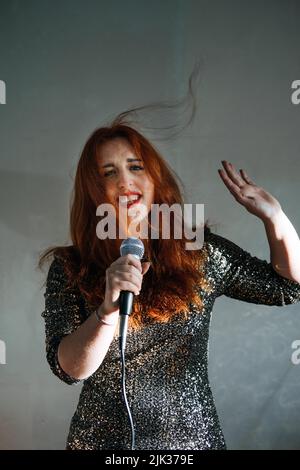 Ritratto di donna cantante rossa in abito da sera scintillante che tiene il microfono Foto Stock