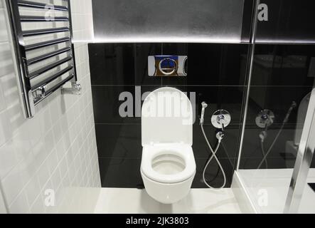 un moderno gabinetto bianco e nero, bagno con vasca da bagno montata a parete, doccia bidet, spruzzatore bidet e portasciugamani riscaldato, radiatore. Foto Stock