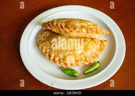 torta di pastie o torta di pasticceria o pastello kue servito con peperoncino verde in un piccolo piatto su sfondo di legno. torta pastello indonesiana Foto Stock