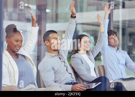 Abbiamo tutti delle domande: Un gruppo di uomini d'affari che si alzano le mani durante una riunione sul lavoro. Foto Stock
